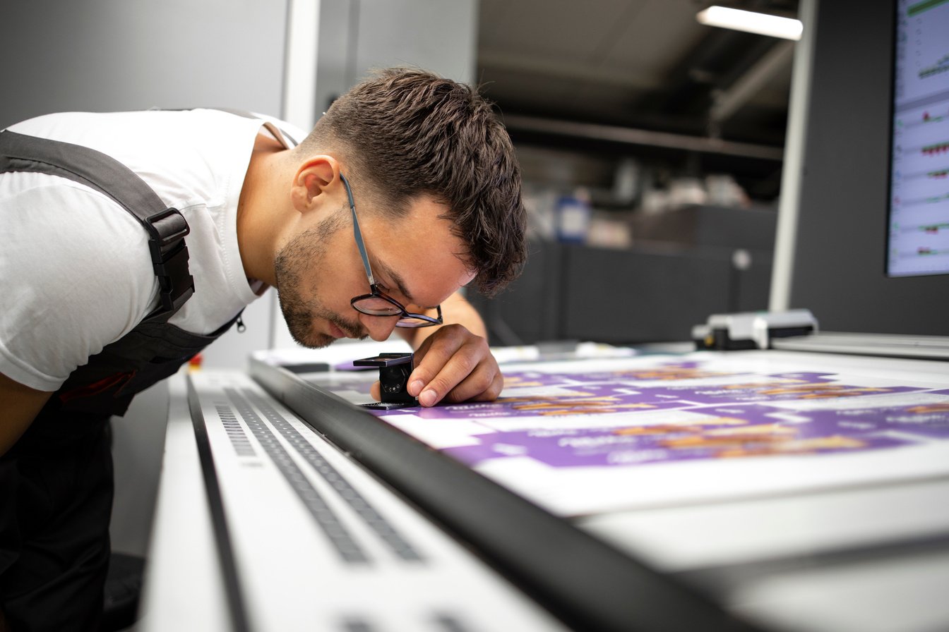 Worker checking print quality of graphics in modern printing house.